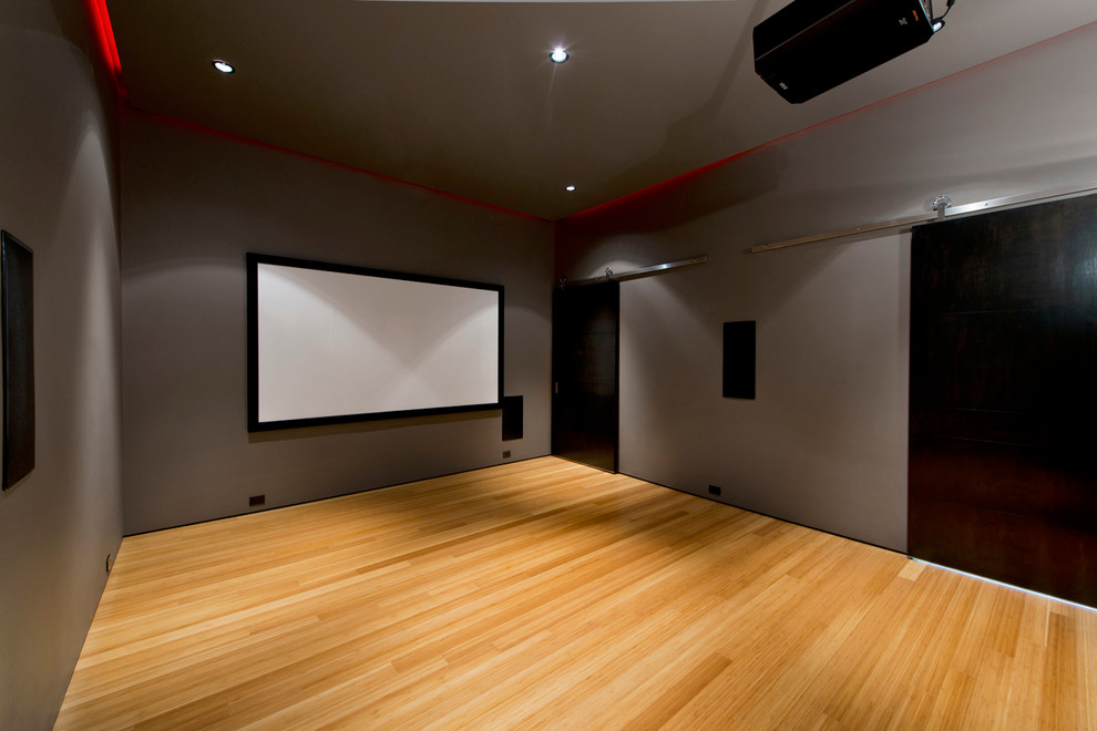 This is an example of a mid-sized contemporary enclosed home theatre in Other with grey walls, bamboo floors and a projector screen.