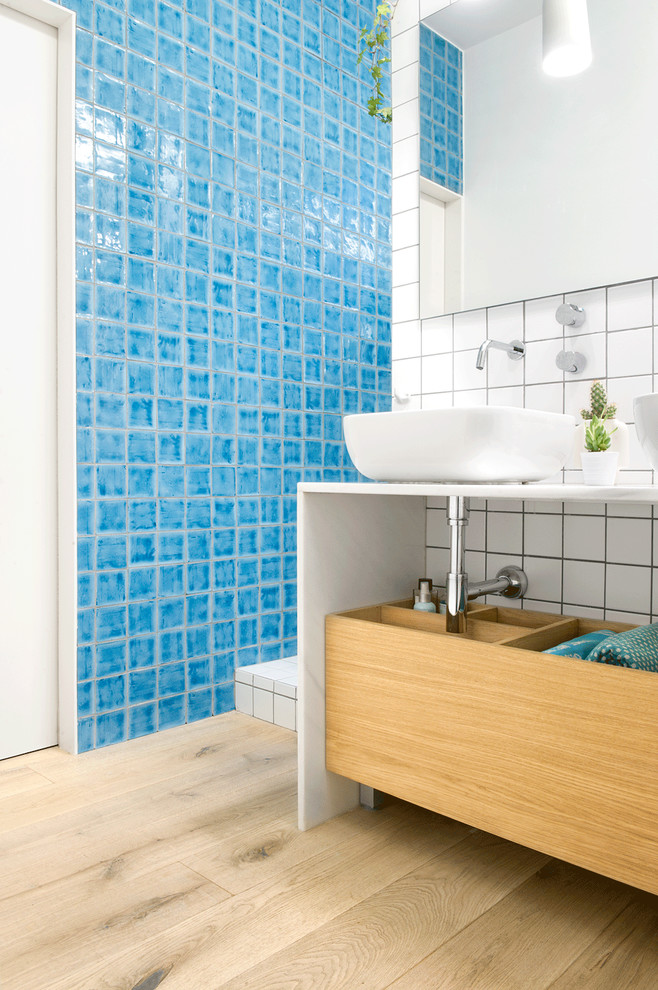 Photo of a mid-sized scandinavian 3/4 bathroom in Madrid with blue tile, flat-panel cabinets, medium wood cabinets, ceramic tile, blue walls, light hardwood floors, a vessel sink and solid surface benchtops.