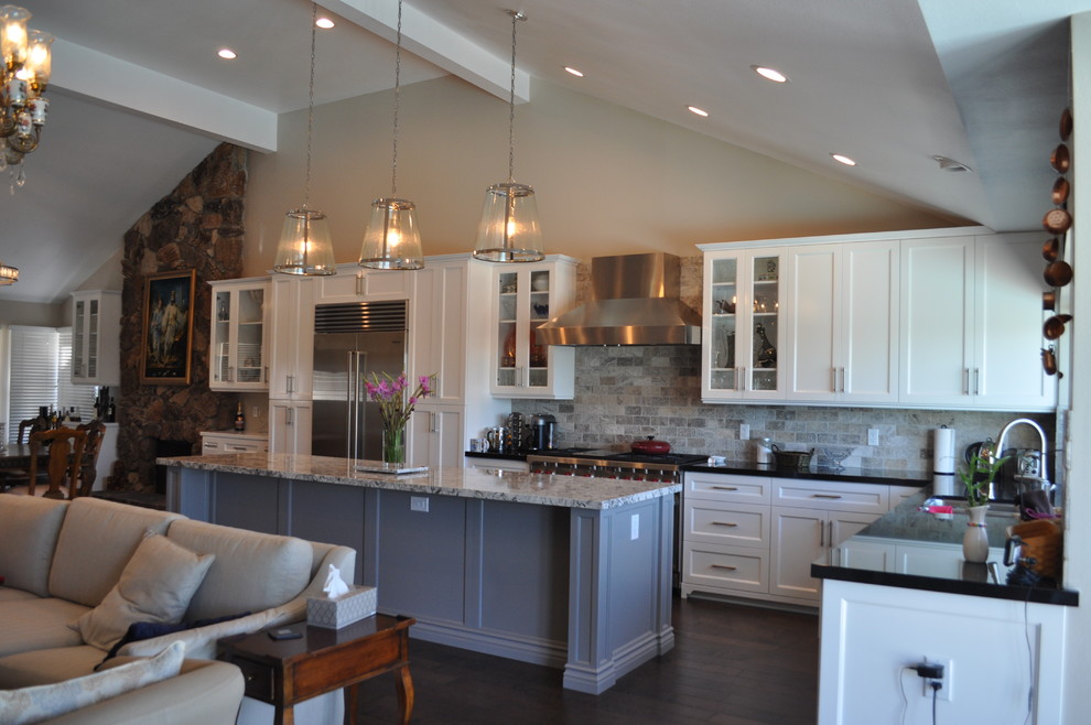 This is an example of a mid-sized transitional l-shaped open plan kitchen in Orange County with a double-bowl sink, shaker cabinets, white cabinets, granite benchtops, grey splashback, stone tile splashback, stainless steel appliances, dark hardwood floors, with island and brown floor.