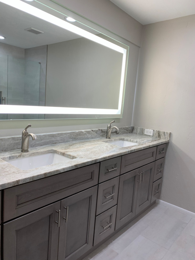 This is an example of a mid-sized modern master bathroom in Jacksonville with shaker cabinets, grey cabinets, an alcove tub, a shower/bathtub combo, a two-piece toilet, gray tile, porcelain tile, grey walls, porcelain floors, an undermount sink, quartzite benchtops, grey floor, a hinged shower door, grey benchtops, a niche, a double vanity and a built-in vanity.