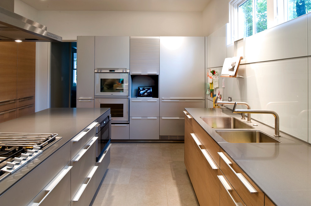 Photo of a large modern u-shaped eat-in kitchen in DC Metro with a double-bowl sink, flat-panel cabinets, stainless steel cabinets, white splashback, glass sheet splashback, glass benchtops, stainless steel appliances, concrete floors and with island.