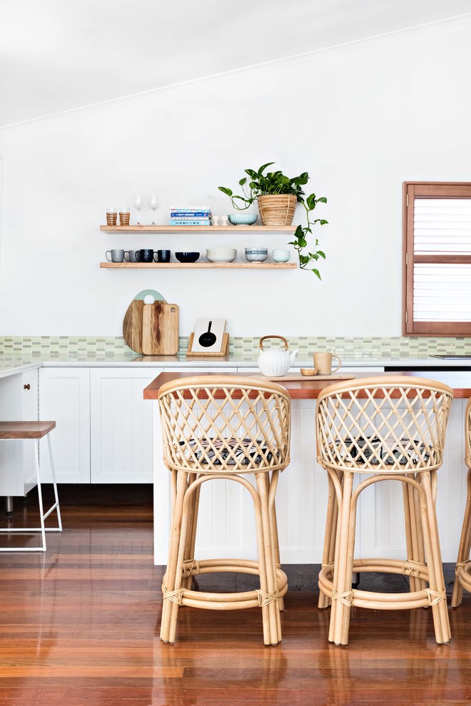Inspiration for a beach style l-shaped kitchen in Wollongong with shaker cabinets, white cabinets, wood benchtops, green splashback, mosaic tile splashback, medium hardwood floors, with island, brown floor and brown benchtop.