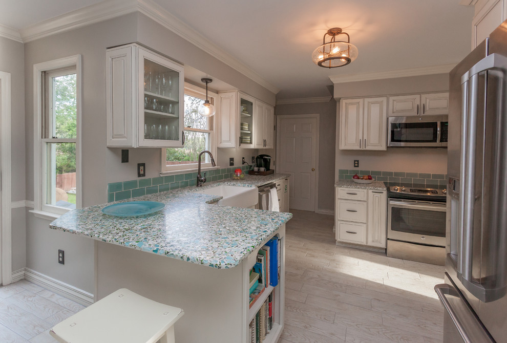This is an example of a mid-sized contemporary u-shaped eat-in kitchen in Charleston with a farmhouse sink, glass-front cabinets, white cabinets, recycled glass benchtops, blue splashback, ceramic splashback, stainless steel appliances and ceramic floors.