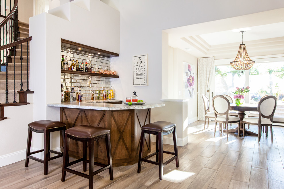 Inspiration for a mediterranean u-shaped seated home bar in San Diego with open cabinets, dark wood cabinets, mirror splashback and light hardwood floors.