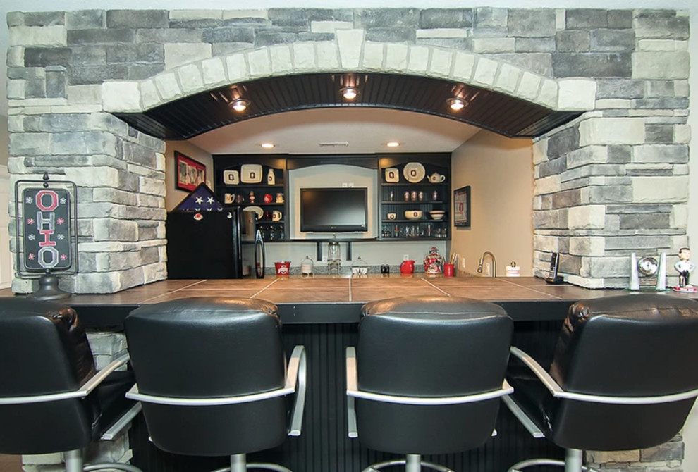 This is an example of a mid-sized transitional u-shaped seated home bar in Other with open cabinets, black cabinets, tile benchtops and beige benchtop.