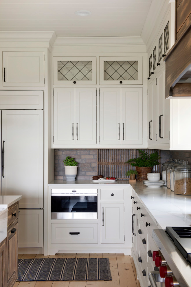 Inspiration for a large country l-shaped kitchen in Minneapolis with a farmhouse sink, white cabinets, multi-coloured splashback, brick splashback, stainless steel appliances, with island and white benchtop.