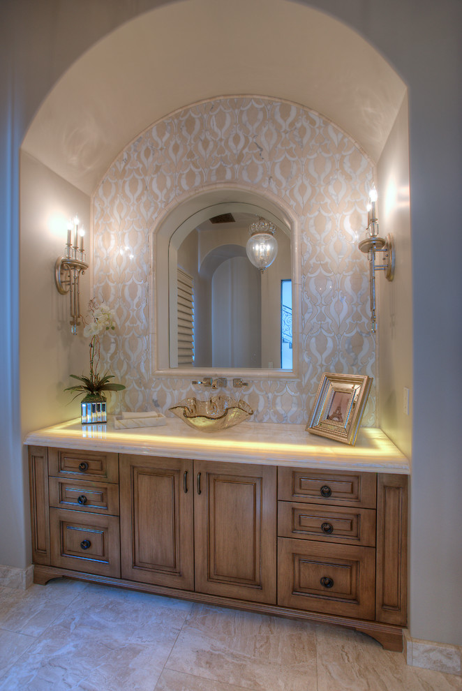Photo of an expansive mediterranean powder room in Phoenix with furniture-like cabinets, medium wood cabinets, a one-piece toilet, beige tile, mosaic tile, white walls, a vessel sink, onyx benchtops, porcelain floors and white floor.