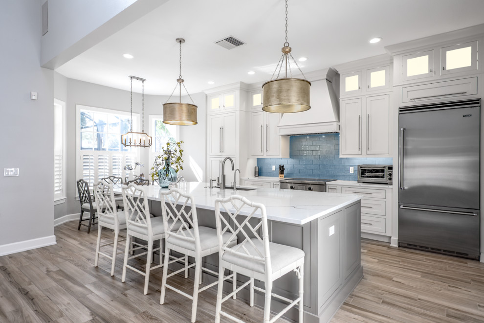 Design ideas for a mid-sized contemporary single-wall eat-in kitchen in Tampa with an undermount sink, shaker cabinets, white cabinets, quartz benchtops, blue splashback, glass sheet splashback, stainless steel appliances, porcelain floors, with island, grey floor and white benchtop.