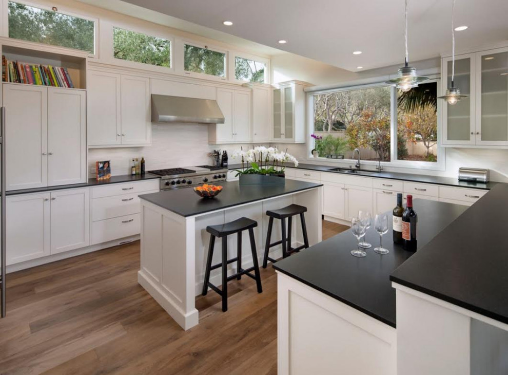 Kitchen - large transitional medium tone wood floor and brown floor kitchen idea in Denver with an undermount sink, shaker cabinets, white cabinets, granite countertops, white backsplash, stone tile backsplash, stainless steel appliances, two islands and black countertops