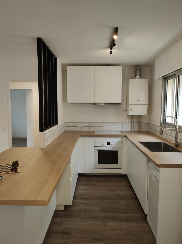 This is an example of a medium sized scandinavian u-shaped kitchen/diner in Nice with a single-bowl sink, flat-panel cabinets, white cabinets, laminate countertops, white splashback, metro tiled splashback, white appliances, vinyl flooring, an island and brown floors.