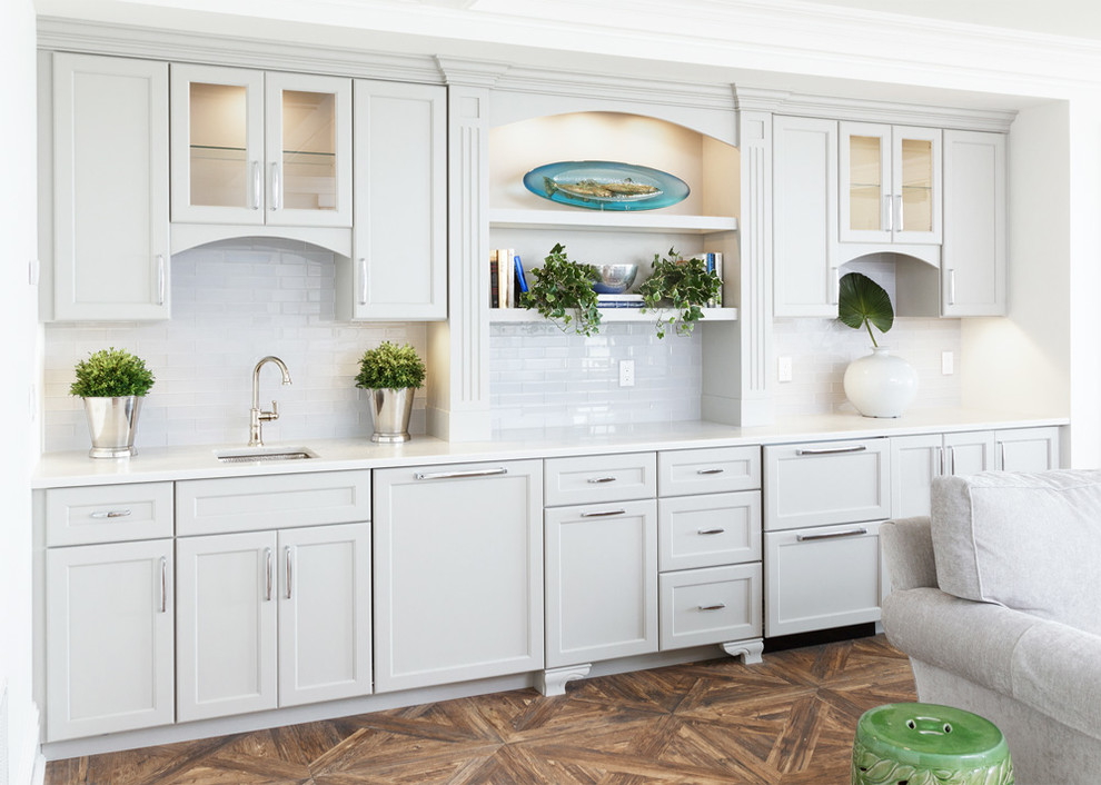 Inspiration for a mid-sized transitional single-wall wet bar in New York with an undermount sink, recessed-panel cabinets, white cabinets, white splashback, subway tile splashback, medium hardwood floors and marble benchtops.