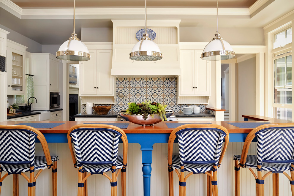 Photo of a large beach style single-wall open plan kitchen in San Diego with a farmhouse sink, beaded inset cabinets, white cabinets, soapstone benchtops, blue splashback, cement tile splashback, panelled appliances, light hardwood floors, with island and multi-coloured floor.