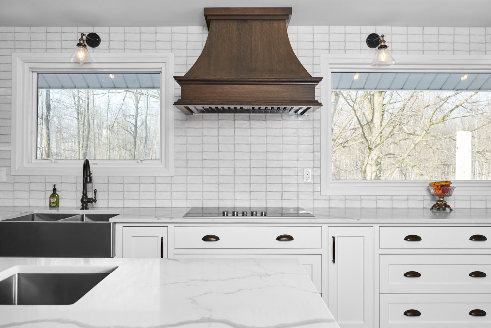 Transitional galley light wood floor and brown floor enclosed kitchen photo in Toronto with a farmhouse sink, shaker cabinets, white cabinets, quartzite countertops, white backsplash, subway tile backsplash, stainless steel appliances, an island and white countertops