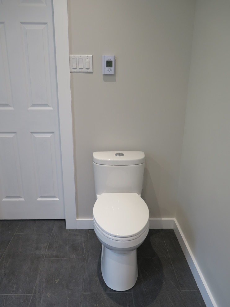 Photo of a mid-sized transitional powder room in Montreal with furniture-like cabinets, white cabinets, a one-piece toilet, gray tile, porcelain tile, grey walls, ceramic floors, a console sink and grey floor.