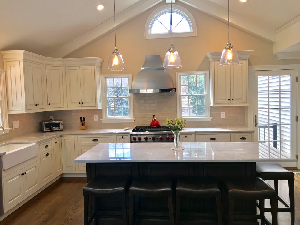 Photo of an expansive traditional l-shaped eat-in kitchen in New York with a farmhouse sink, beaded inset cabinets, white cabinets, quartzite benchtops, grey splashback, glass tile splashback, stainless steel appliances, medium hardwood floors, with island and brown floor.