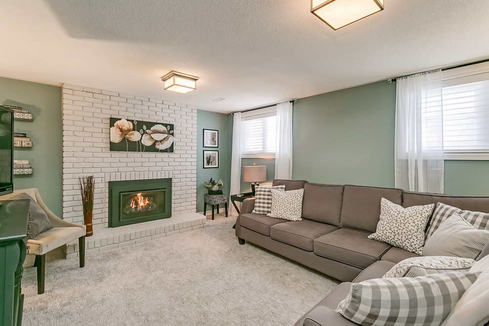 Photo of a small transitional look-out basement in Toronto with green walls, carpet, a standard fireplace, a brick fireplace surround and grey floor.