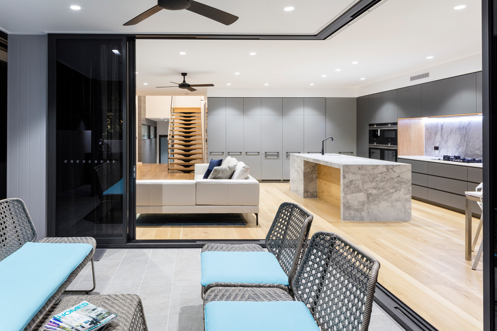 Photo of a mid-sized contemporary galley open plan kitchen in Brisbane with an undermount sink, flat-panel cabinets, grey cabinets, marble benchtops, grey splashback, marble splashback, black appliances, light hardwood floors, with island and grey benchtop.