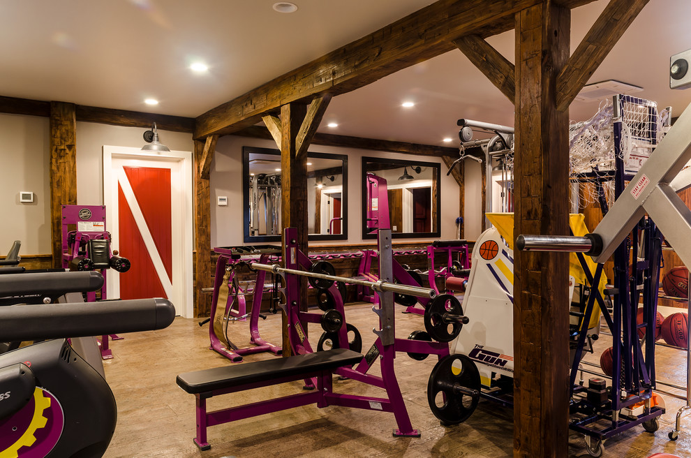 This is an example of a large country home weight room in New York with beige walls and light hardwood floors.