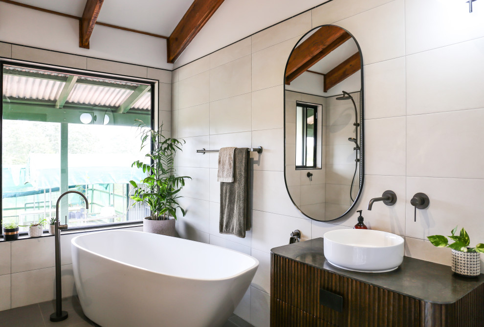 This is an example of a large contemporary master bathroom in Other with dark wood cabinets, a freestanding tub, beige tile, ceramic tile, white walls, ceramic floors, a vessel sink, soapstone benchtops, an open shower, a single vanity, a floating vanity, vaulted, exposed beam, flat-panel cabinets, grey floor and grey benchtops.