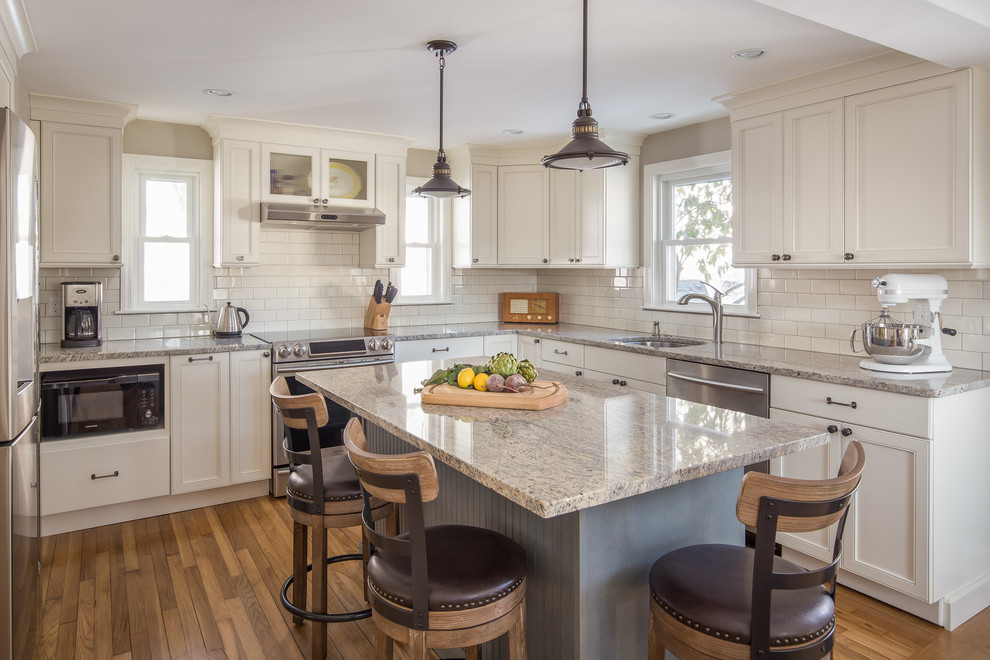 Photo of a mid-sized traditional u-shaped eat-in kitchen in Boston with an undermount sink, white cabinets, granite benchtops, subway tile splashback, stainless steel appliances, with island, recessed-panel cabinets, white splashback, medium hardwood floors and brown floor.