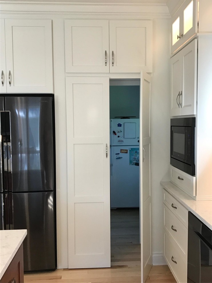 Large transitional l-shaped light wood floor eat-in kitchen photo with an undermount sink, flat-panel cabinets, white cabinets, quartz countertops, white backsplash, subway tile backsplash, stainless steel appliances, an island and white countertops