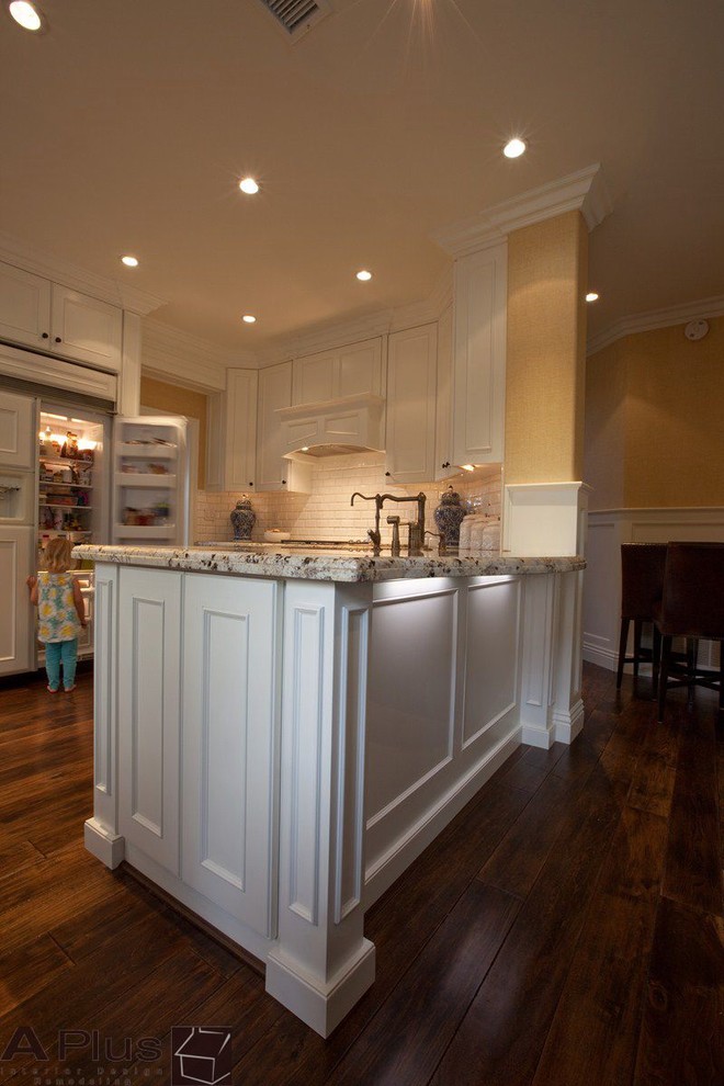 Inspiration for a mid-sized traditional l-shaped eat-in kitchen in Orange County with a farmhouse sink, recessed-panel cabinets, white cabinets, granite benchtops, white splashback, subway tile splashback, panelled appliances, medium hardwood floors and no island.