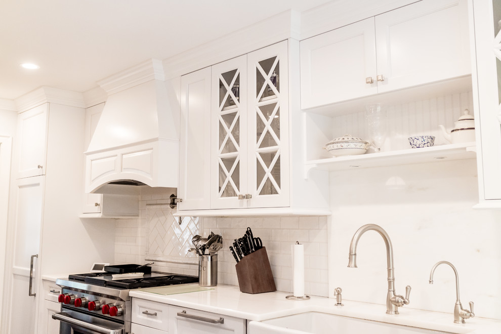 Enclosed kitchen - mid-sized transitional dark wood floor and brown floor enclosed kitchen idea in New York with a farmhouse sink, recessed-panel cabinets, white cabinets, quartzite countertops, white backsplash, subway tile backsplash, stainless steel appliances and an island