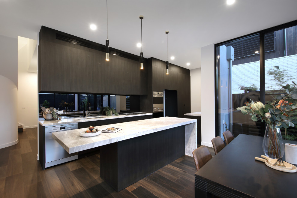Photo of a mid-sized contemporary single-wall open plan kitchen in Melbourne with a drop-in sink, flat-panel cabinets, brown cabinets, quartz benchtops, multi-coloured splashback, glass tile splashback, stainless steel appliances, dark hardwood floors, with island, brown floor and white benchtop.