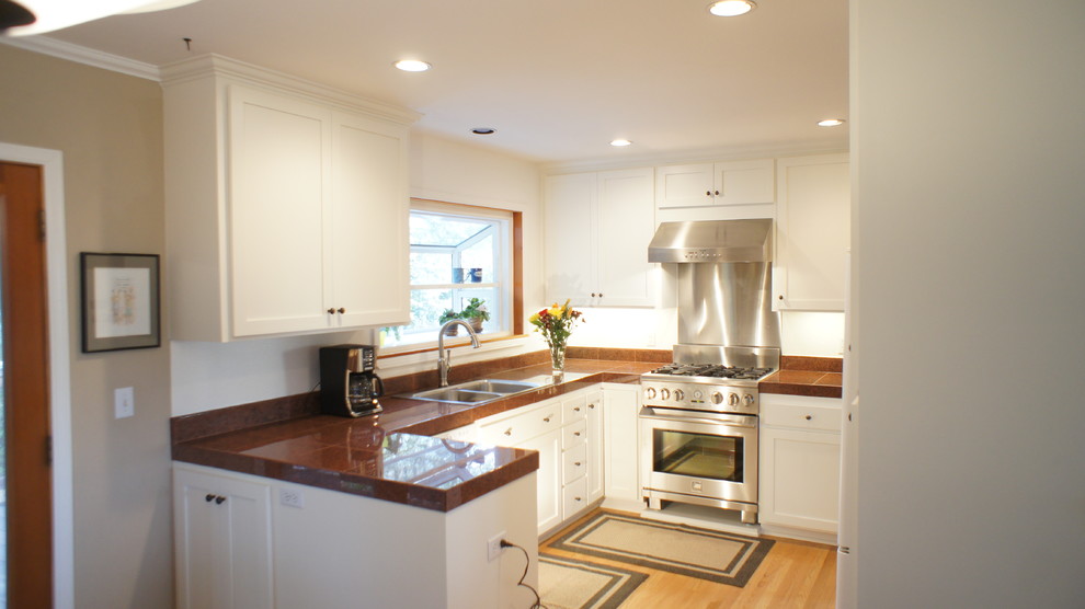 Inspiration for a large transitional u-shaped eat-in kitchen in San Francisco with a double-bowl sink, shaker cabinets, white cabinets, tile benchtops, white splashback, stone tile splashback, stainless steel appliances, light hardwood floors and a peninsula.