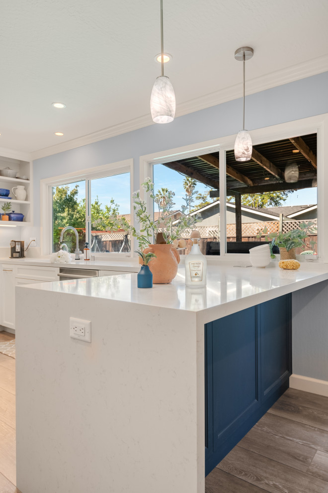 Inspiration for a mid-sized contemporary l-shaped eat-in kitchen in San Francisco with an undermount sink, shaker cabinets, white cabinets, quartzite benchtops, white splashback, porcelain splashback, stainless steel appliances, vinyl floors, a peninsula, brown floor and white benchtop.