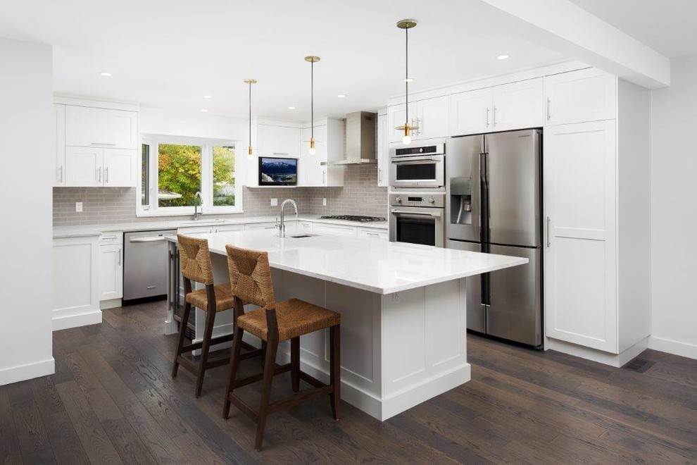 Inspiration for a mid-sized transitional l-shaped dark wood floor and brown floor open concept kitchen remodel in Calgary with an undermount sink, shaker cabinets, white cabinets, quartz countertops, gray backsplash, subway tile backsplash, stainless steel appliances and an island