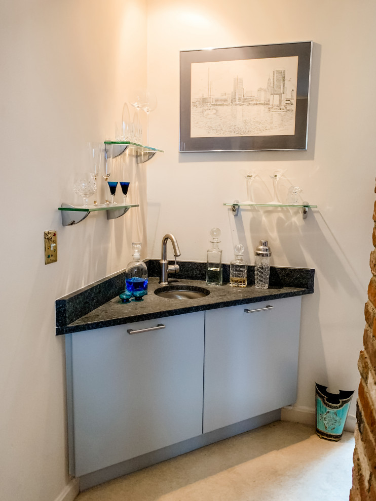 Photo of a small transitional single-wall wet bar in DC Metro with flat-panel cabinets, an undermount sink, grey cabinets, granite benchtops, black splashback, granite splashback, carpet, beige floor and black benchtop.