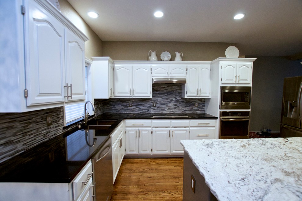 Kitchen - large transitional l-shaped medium tone wood floor kitchen idea with a double-bowl sink, raised-panel cabinets, white cabinets, solid surface countertops, multicolored backsplash, matchstick tile backsplash, stainless steel appliances and an island