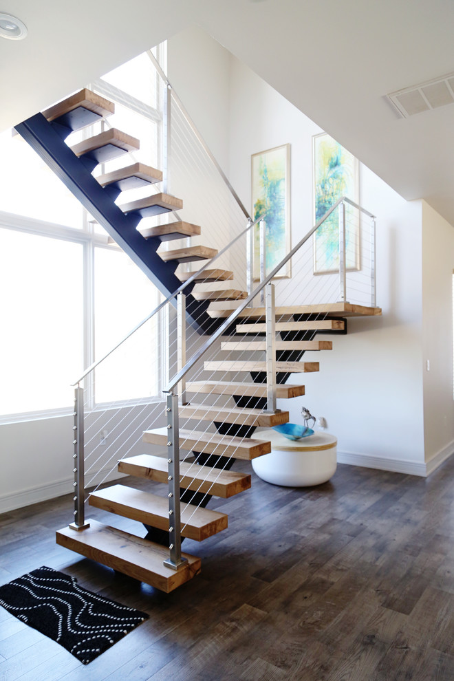 Lake House Dream - Floating staircase picture taken after client move in. Front focal stairway that provides access from a large open expansive downstairs living to the upstairs bedrooms, deck and game room. HSS Structural steel support hidden in walls with solid white oak treads and stainless steel handrails and cable. LED lights were installed in the nosing of the stairs. Bona-Waterborne Traffic Naturale finish used on stairs for natural color, matte finish level and seamless touch-up on repairs. Furnishings, interior selections and artwork by Susan Eddings Perez