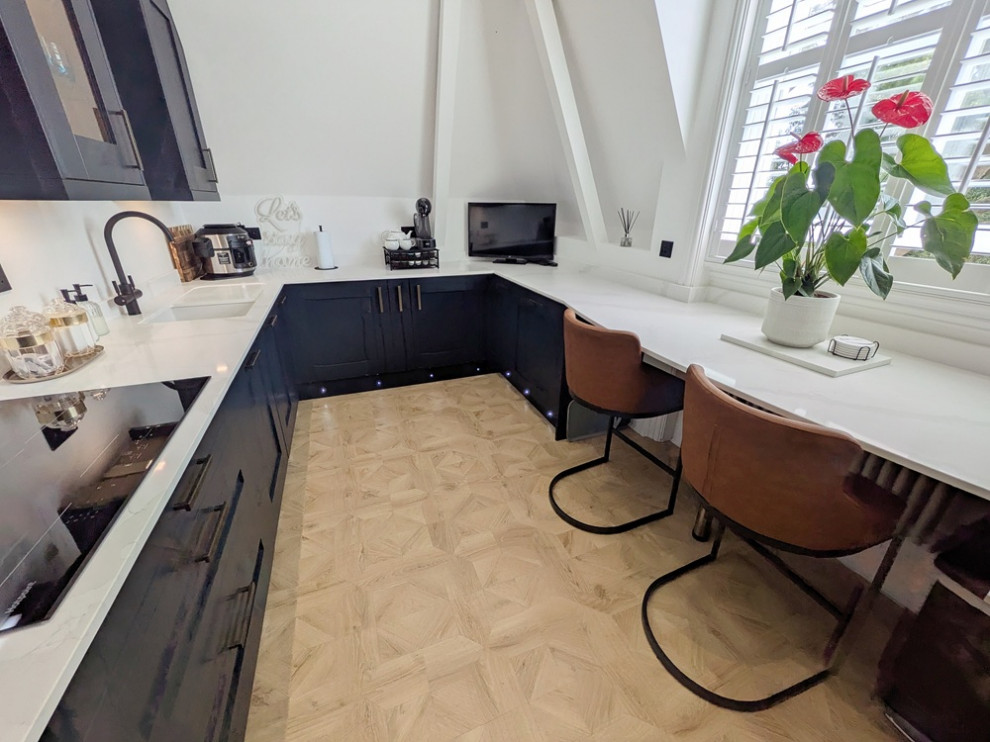 Photo of a medium sized traditional galley enclosed kitchen in West Midlands with an integrated sink, shaker cabinets, blue cabinets, quartz worktops, white splashback, integrated appliances, laminate floors, a breakfast bar, brown floors, white worktops and feature lighting.