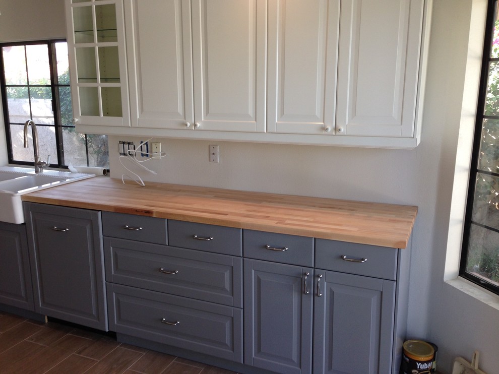 Example of a transitional u-shaped laminate floor and brown floor enclosed kitchen design with a farmhouse sink, shaker cabinets, white cabinets, wood countertops, white backsplash, subway tile backsplash and stainless steel appliances