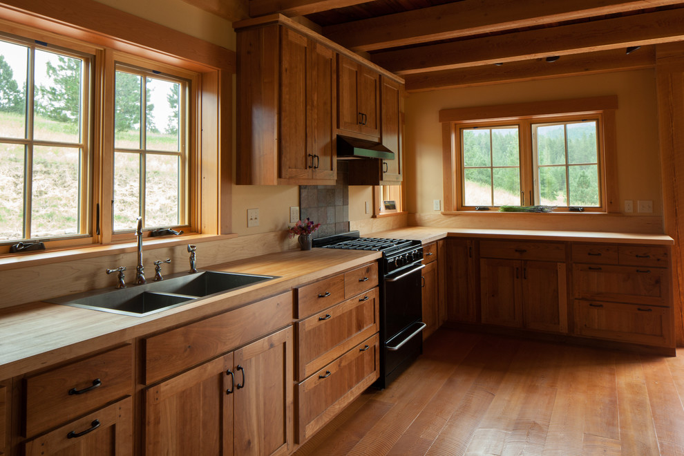 Example of a mid-sized mountain style l-shaped medium tone wood floor open concept kitchen design with a drop-in sink, flat-panel cabinets, medium tone wood cabinets, wood countertops and black appliances