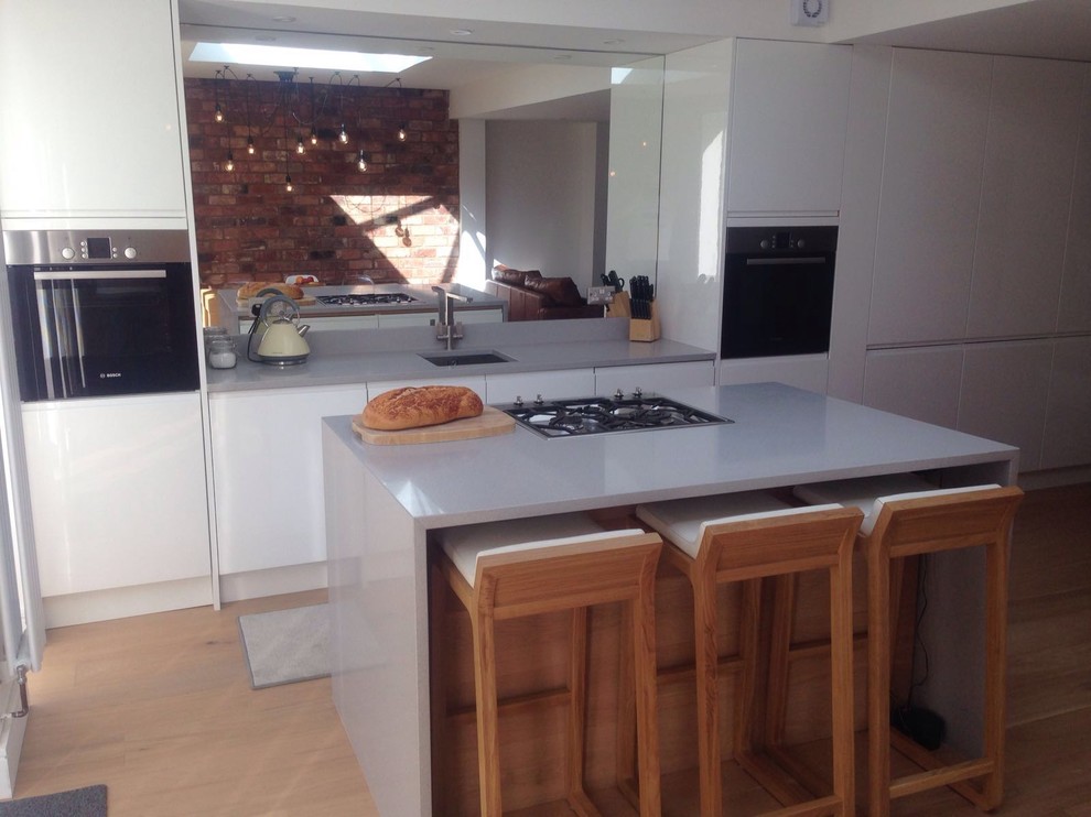 This is an example of a medium sized modern single-wall open plan kitchen in West Midlands with a built-in sink, flat-panel cabinets, white cabinets, granite worktops, mirror splashback, laminate floors, an island and brown floors.
