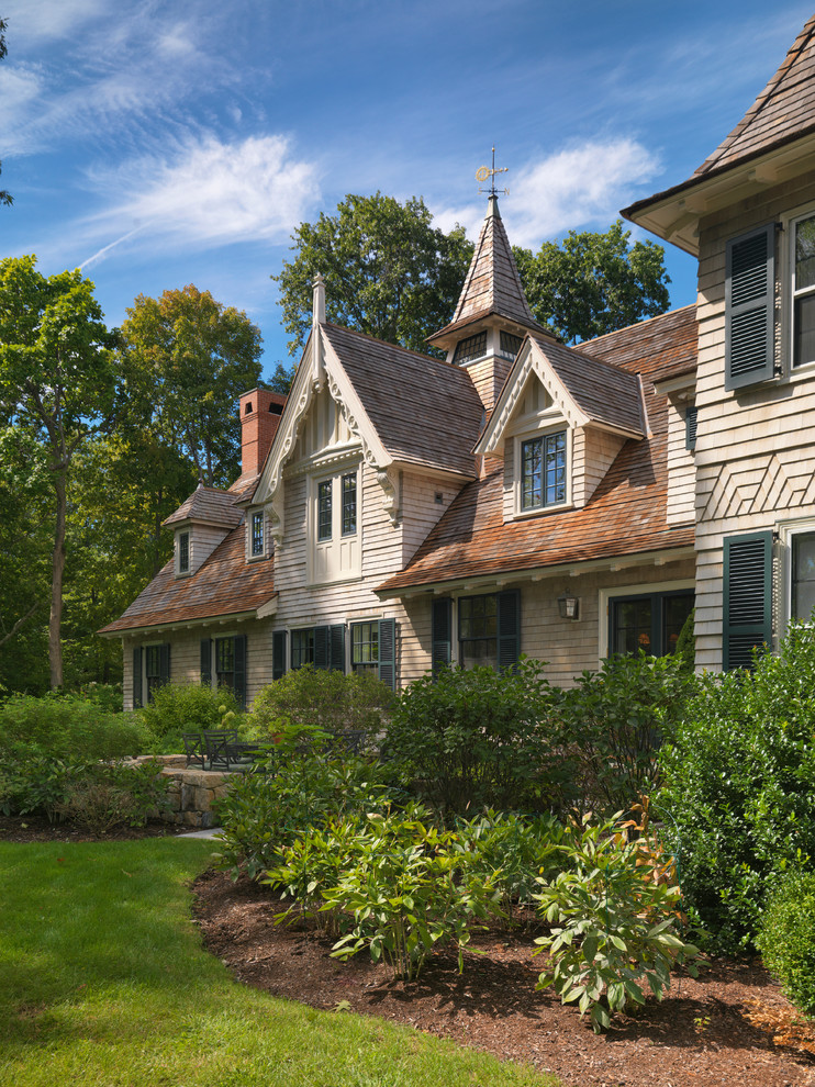 This is an example of a large traditional three-storey beige house exterior in Boston with wood siding and a gable roof.
