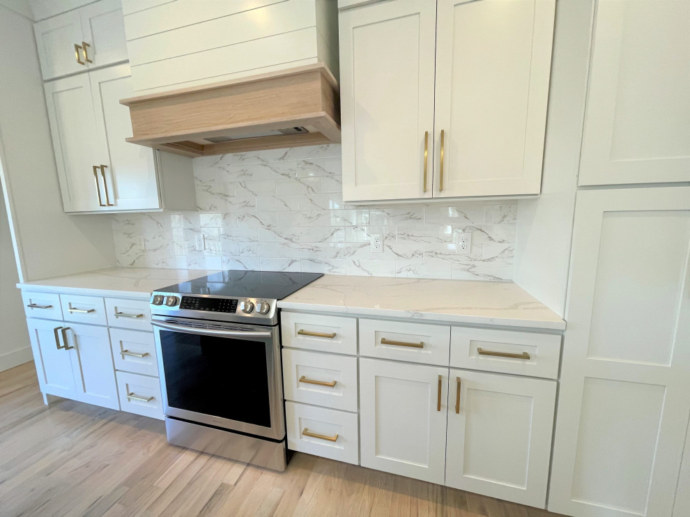 Mid-sized transitional single-wall eat-in kitchen photo with a farmhouse sink, shaker cabinets, white cabinets, quartz countertops, white backsplash, marble backsplash, stainless steel appliances, an island and white countertops