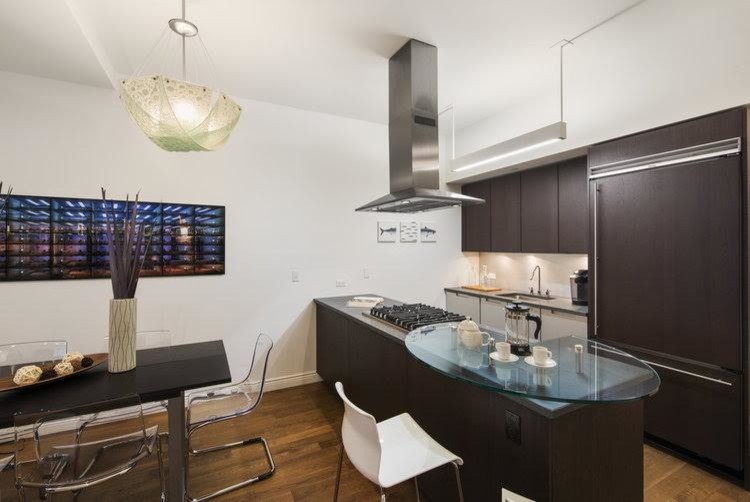 Photo of a small contemporary galley eat-in kitchen with an undermount sink, flat-panel cabinets, dark wood cabinets, stainless steel benchtops, white splashback, stainless steel appliances, medium hardwood floors, with island and brown floor.