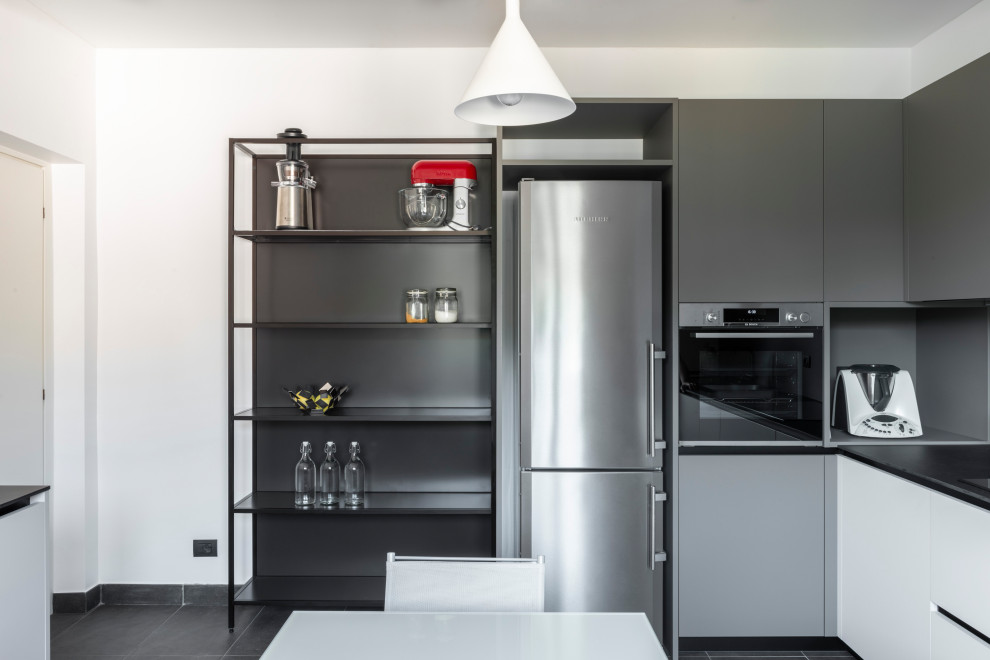 Diseño de cocinas en L minimalista grande cerrada sin isla con armarios con paneles lisos, salpicadero negro, suelo gris y encimeras negras