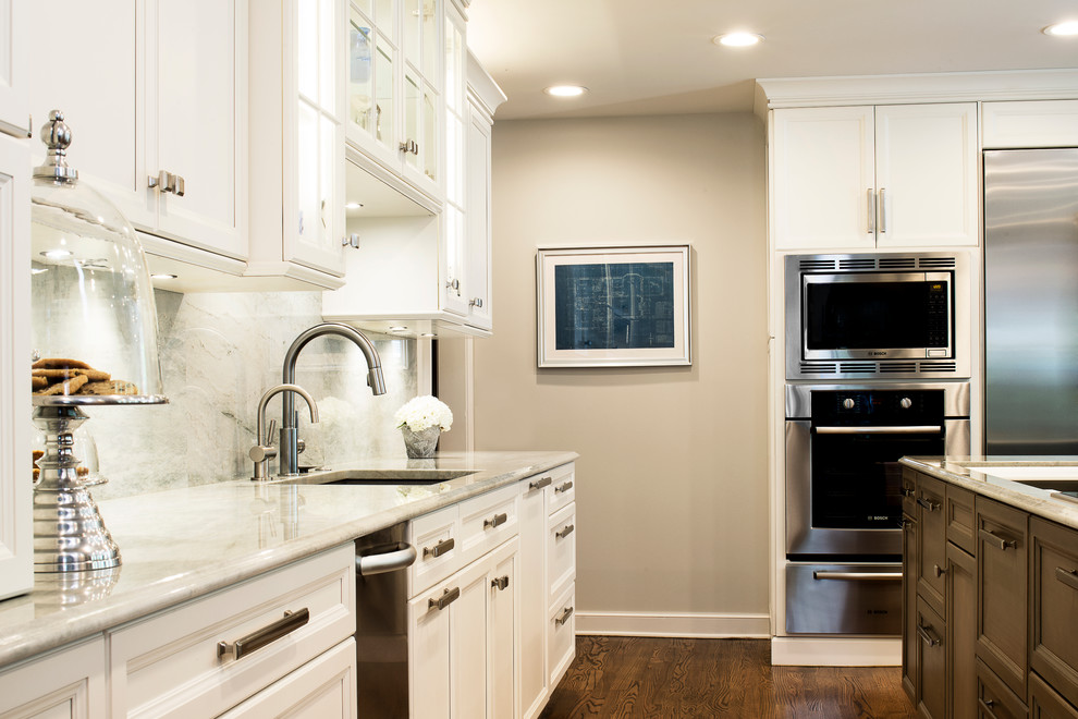 Example of a large transitional single-wall medium tone wood floor and brown floor kitchen design in Denver with an undermount sink, recessed-panel cabinets, white cabinets, white backsplash, stone slab backsplash, stainless steel appliances and an island