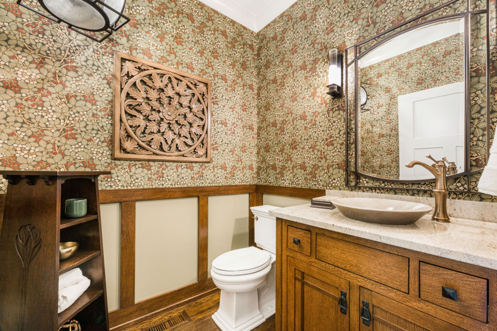 Photo of a medium sized traditional cloakroom in Chicago with freestanding cabinets, medium wood cabinets, a two-piece toilet, multi-coloured walls, medium hardwood flooring, a vessel sink, brown floors, beige worktops, a freestanding vanity unit, wallpapered walls, granite worktops and a dado rail.