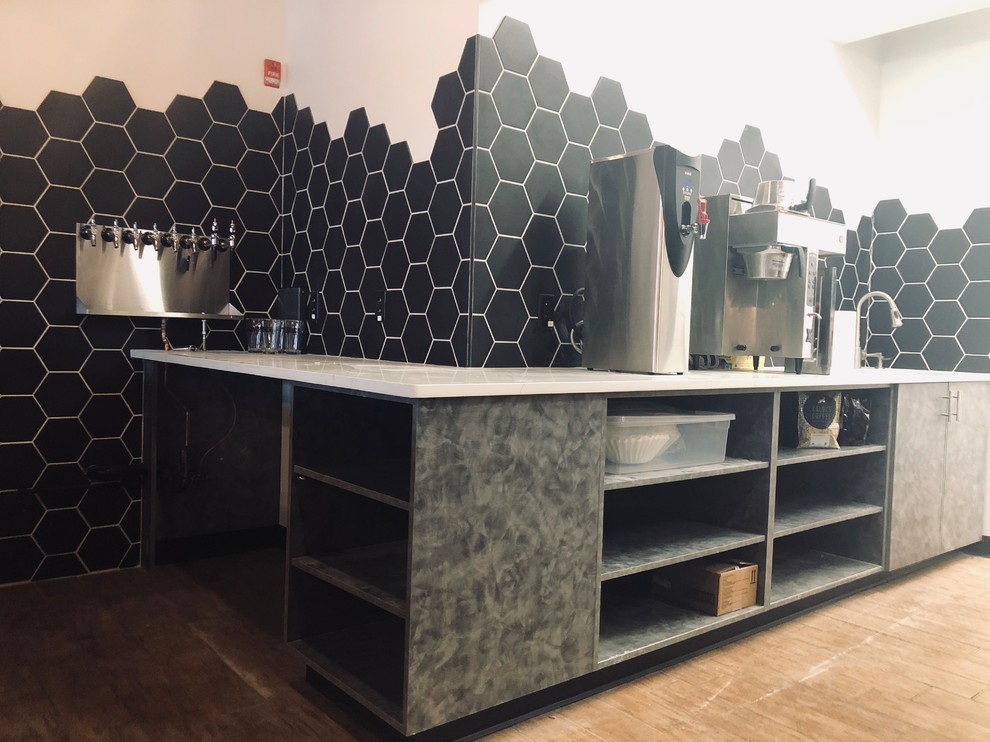 Design ideas for a large industrial l-shaped seated home bar in Omaha with a drop-in sink, open cabinets, grey cabinets, onyx benchtops, black splashback, ceramic splashback, brown floor, white benchtop and ceramic floors.