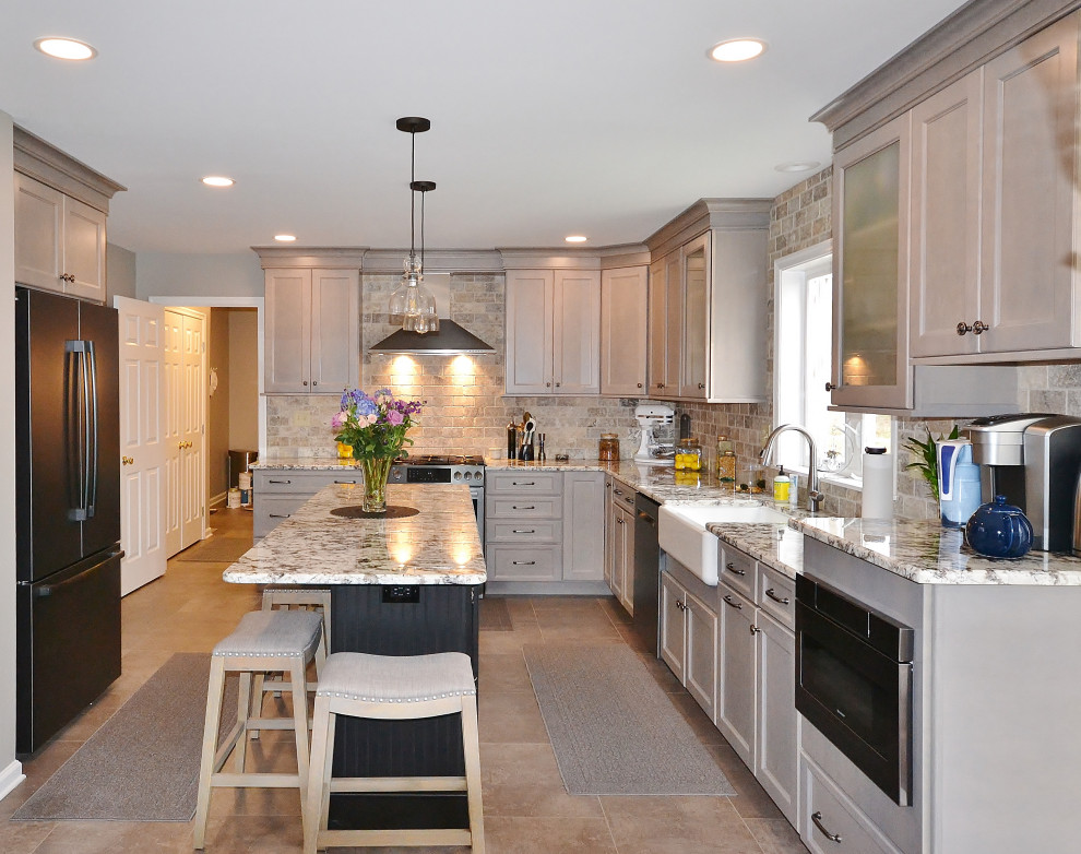 Inspiration for a large transitional l-shaped eat-in kitchen in Philadelphia with a farmhouse sink, raised-panel cabinets, grey cabinets, granite benchtops, beige splashback, travertine splashback, stainless steel appliances, vinyl floors, with island, beige floor and multi-coloured benchtop.