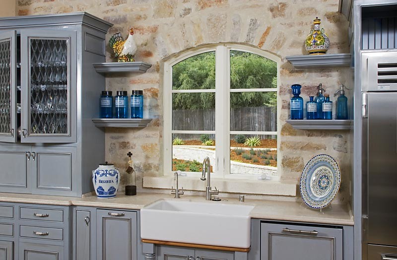 This is an example of an u-shaped kitchen pantry in Other with a farmhouse sink, blue cabinets, limestone benchtops, beige splashback, stone tile splashback, stainless steel appliances and light hardwood floors.