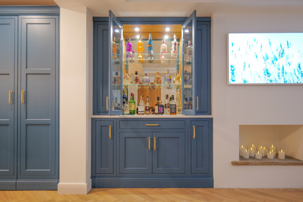 This is an example of a large country u-shaped dry bar with no sink, louvered cabinets, blue cabinets, quartz worktops, multi-coloured splashback, mirror splashback, medium hardwood flooring, brown floors, white worktops and feature lighting.