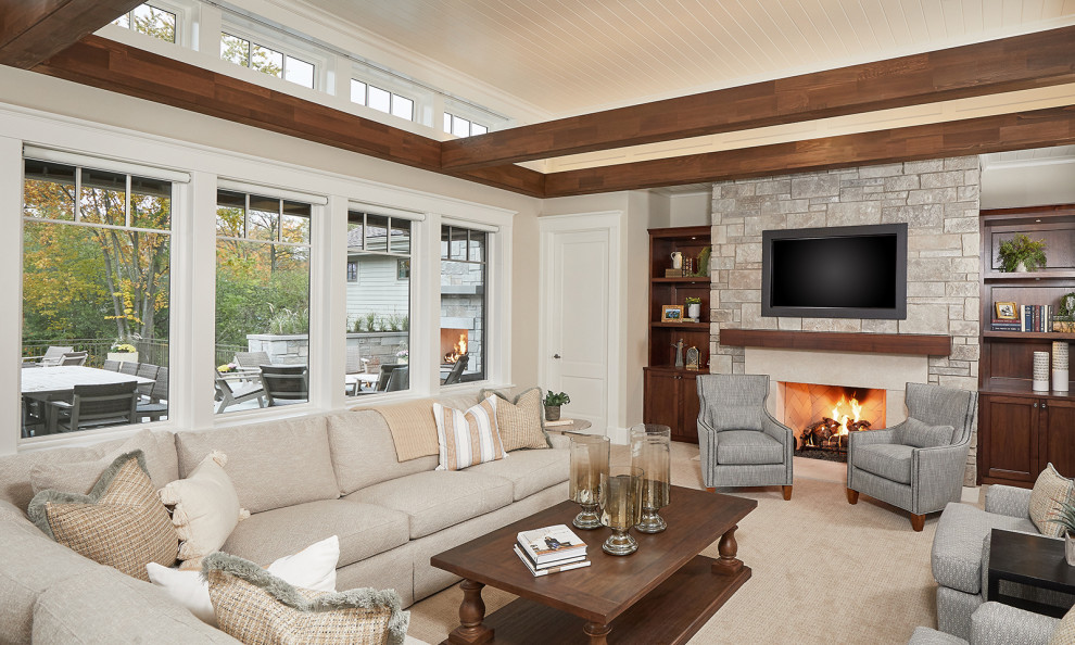 This is an example of a traditional open concept family room in Grand Rapids with beige walls, carpet, a standard fireplace, a stone fireplace surround, a wall-mounted tv and beige floor.