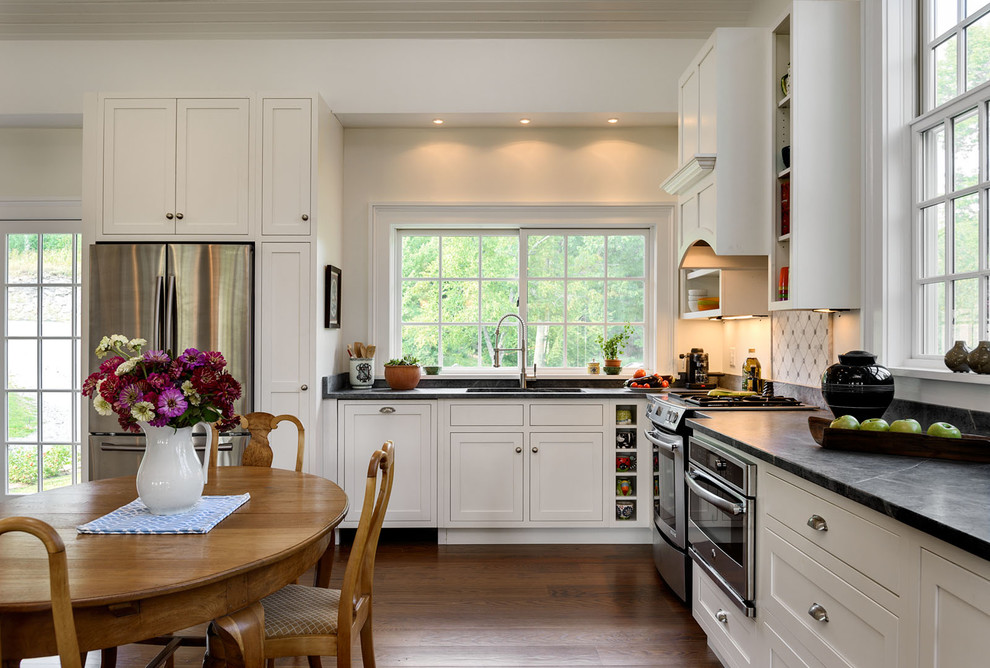 Photo of a mid-sized country l-shaped open plan kitchen in New York with an undermount sink, shaker cabinets, white cabinets, grey splashback, dark hardwood floors, no island, soapstone benchtops, ceramic splashback and stainless steel appliances.